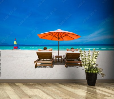 Fototapeta Para na tropikalnej plaży na leżakach pod czerwonym parasolem