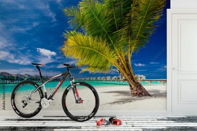 Fototapeta Palma na plaży przed tropikalnymi domkami na palach