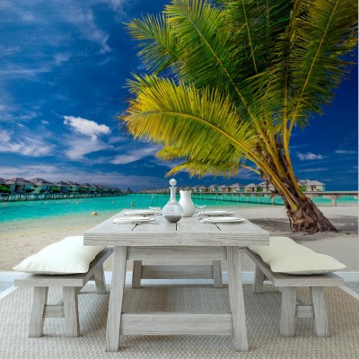 Fototapeta Palma na plaży przed tropikalnymi domkami na palach