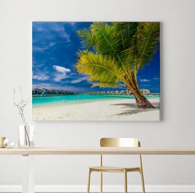 Obraz na płótnie Palma na plaży przed tropikalnymi domkami na palach